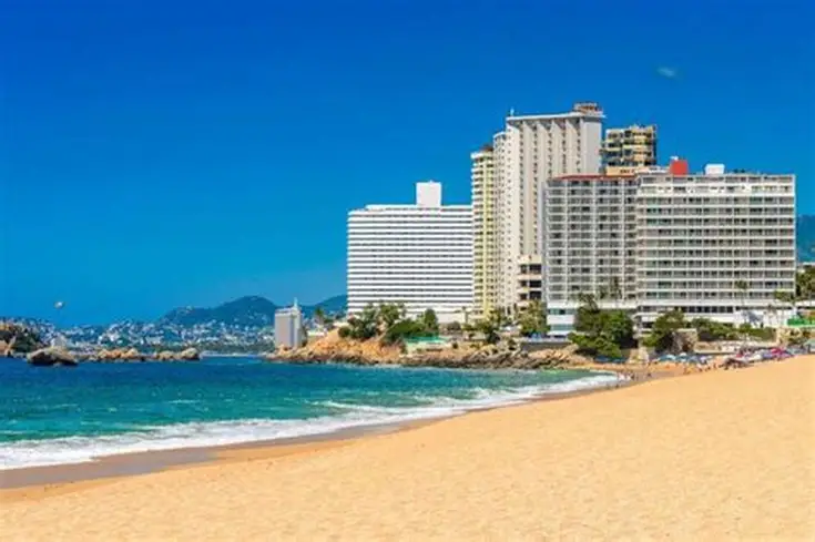 "Panoramic view of Acapulco Bay with high-rise hotels, anchored boats, and golden shoreline curving along the coast."