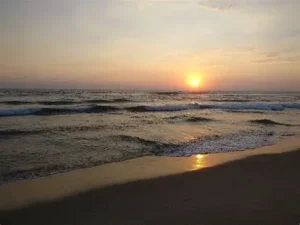 Long stretch of sand at Barra Vieja Beach with beachfront palapas and strong Pacific surf under a golden sky.