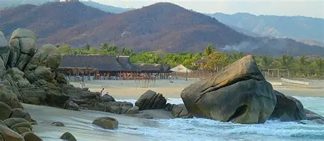 Towering white rock formation at Playa Roca Blanca with crashing waves and sunset glow near Chacahua